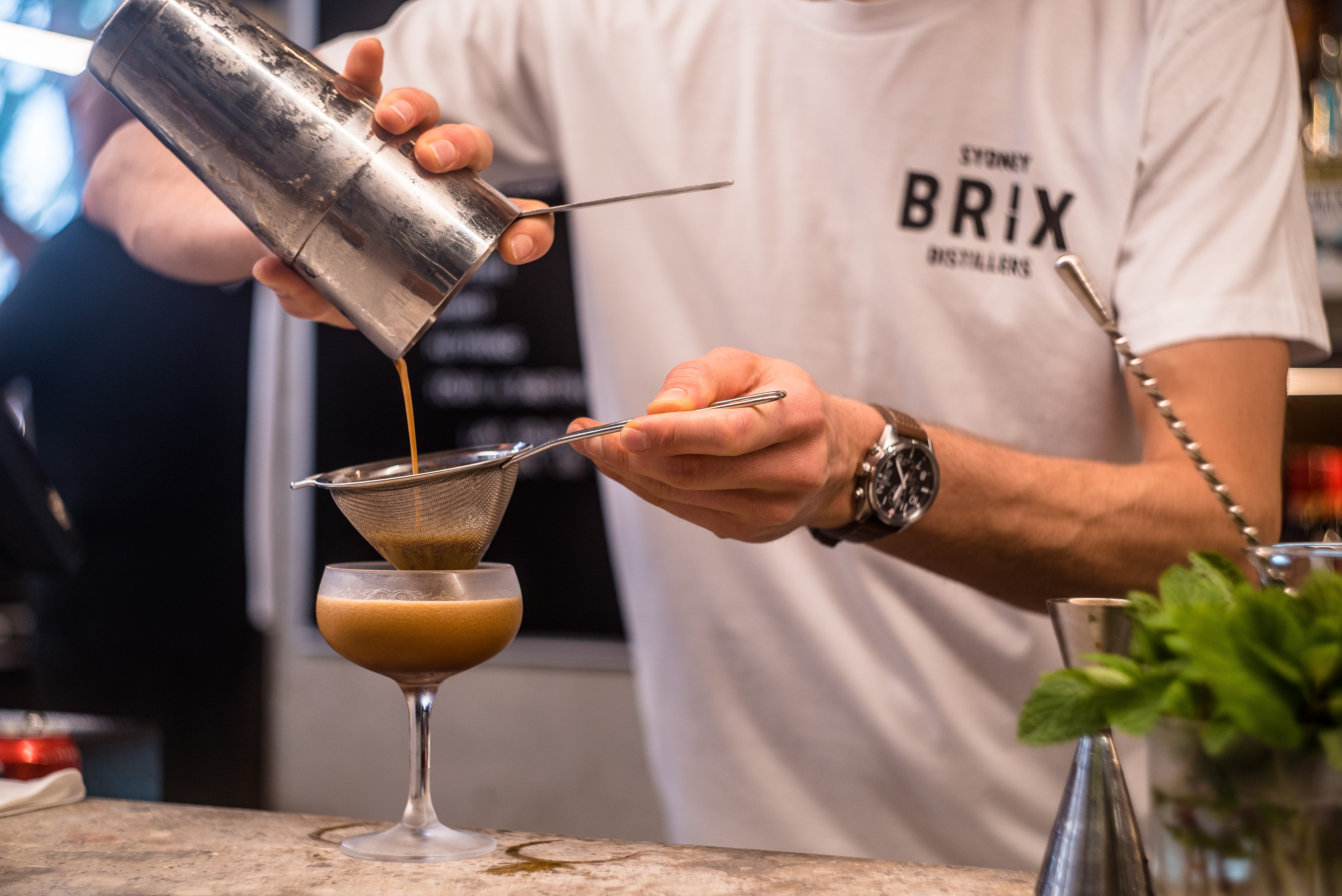 A person is pouring a yellow cocktail through a strainer into a glass